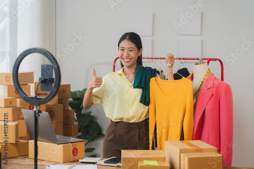 Confidently Launching Her Brand: A young Asian woman entrepreneur, beaming with enthusiasm, films her latest product showcase in her bustling home office. Surrounded by boxes and a backdrop of clothin photo