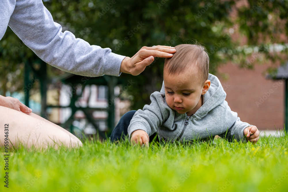 Infant in Grey Hoodie Exploring Green Grass With mother in Park Setting on a Calm Day Infant in Grey Hoodie Exploring Green Grass With mother in Park Setting on a Calm Day