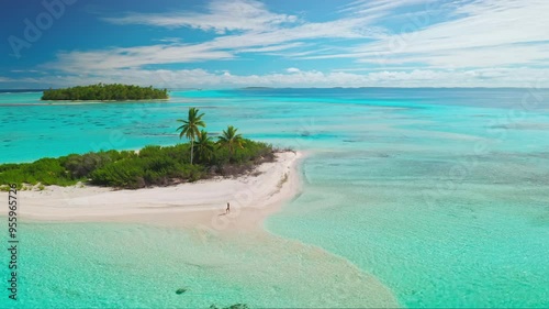 Aerial drone view of a woman walking on a pristine sandy beach with turquoise water and palm trees on a small island in the maldives
