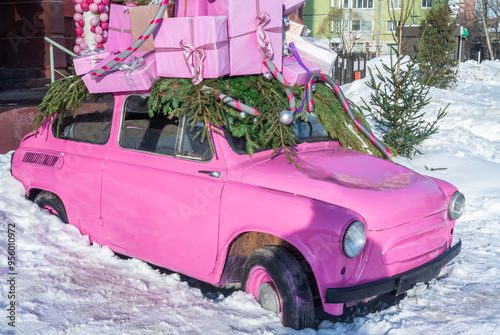 A pink subcompact in a snowdrift with New Year's gifts on the roof. A festive little car. A passenger car in the snow with Christmas gifts. photo