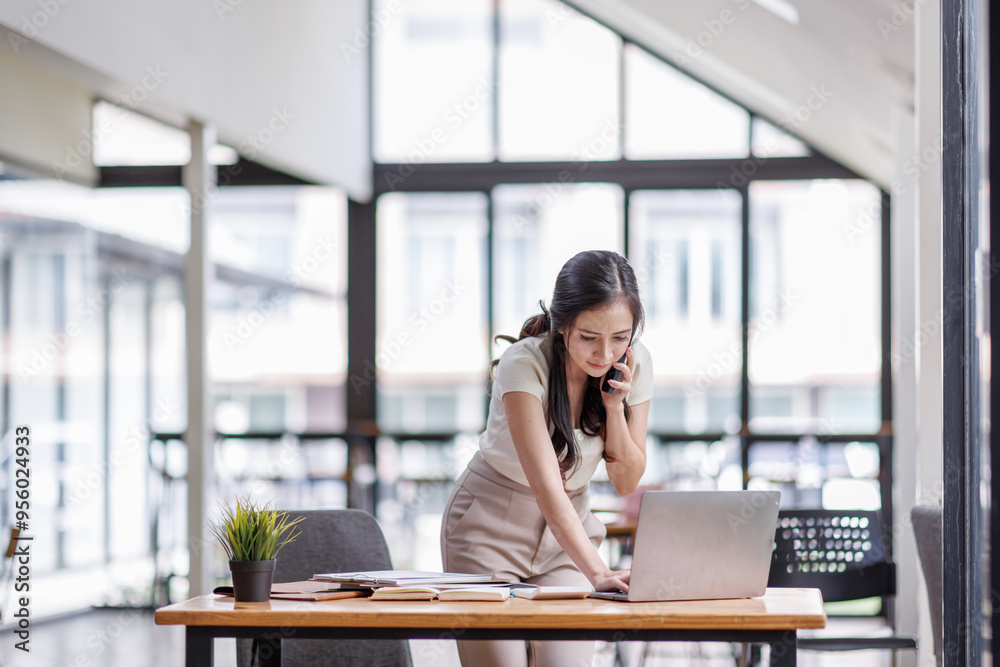 Smiling asian female hold cell at ear talk look at laptop screen. Busy young asian lady advisor lawyer give phone consultation from workplace discuss electronic document details Smiling asian female hold cell at ear talk look at laptop screen. Busy young asian lady advisor lawyer give phone consultation from workplace discuss electronic document details