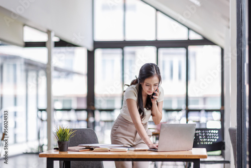Wallpaper Mural Smiling asian female hold cell at ear talk look at laptop screen. Busy young asian lady advisor lawyer give phone consultation from workplace discuss electronic document details Torontodigital.ca