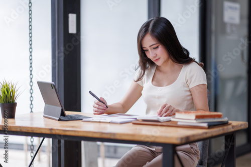 Businesswomen or Asian Accountants using calculator and a tablet laptop computer to analyze business report graphs and finance charts at the workplace, financial and investment concept. 