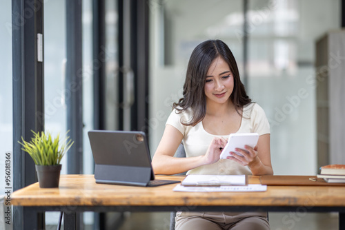 Businesswomen or Asian Accountants using calculator and a tablet laptop computer to analyze business report graphs and finance charts at the workplace, financial and investment concept. 