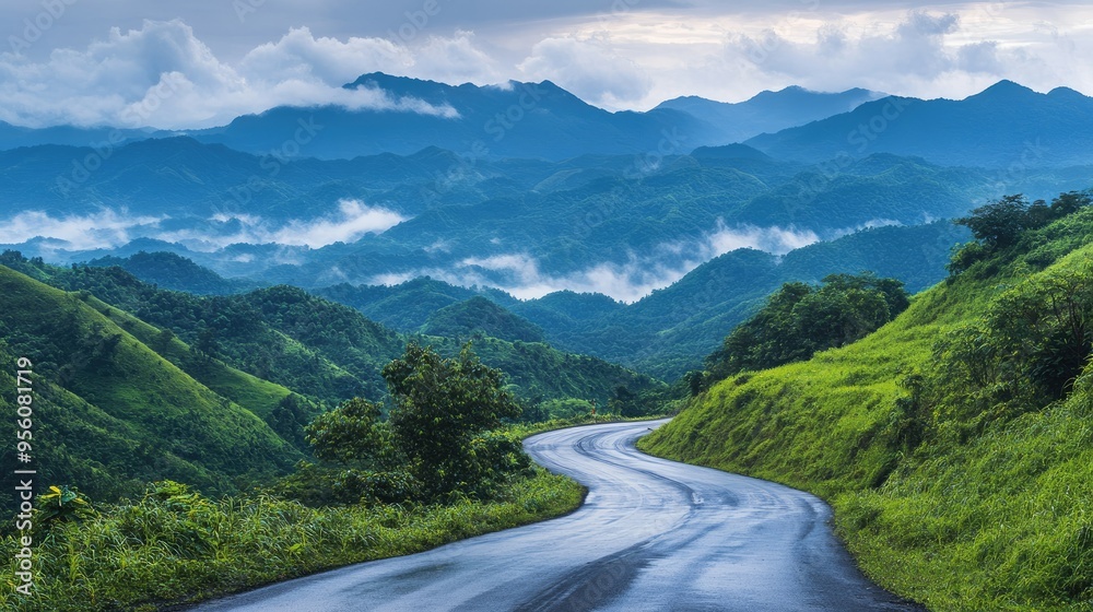 Serene asphalt road curving through lush green mountains, with early morning clouds in the sky Serene asphalt road curving through lush green mountains, with early morning clouds in the sky