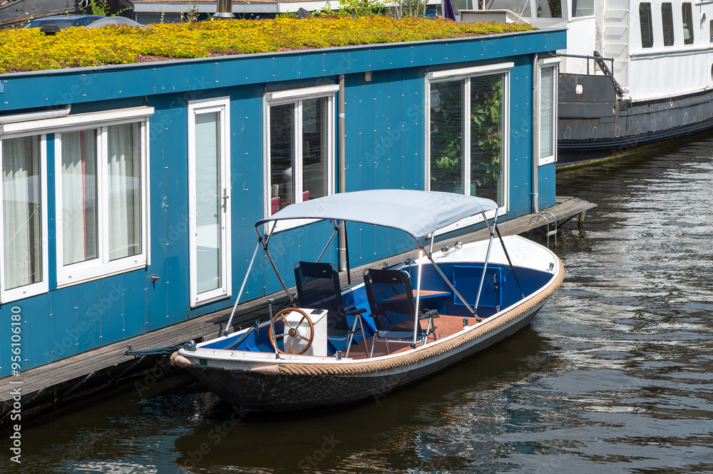 Small motorboat moored next to a blue floating house on a canal. Small motorboat moored next to a blue floating house on a canal.