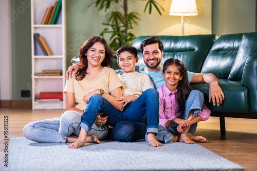 Happy Indian Asian family sitting on the floor with kids in arms, enjoying family time in new home