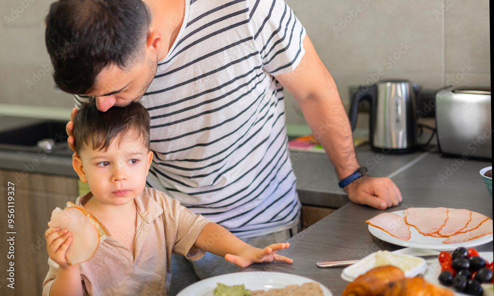 dad and son in modern kitchen eating breakfast.father doing tasty sandwich,smiling happy kid. boy waiting the meal.man kissing child,giving bread with ham.plates with food on counter.morning time dad and son in modern kitchen eating breakfast.father doing tasty sandwich,smiling happy kid. boy waiting the meal.man kissing child,giving bread with ham.plates with food on counter.morning time