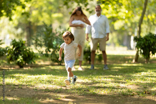 Little boy running ahead of family walking in park