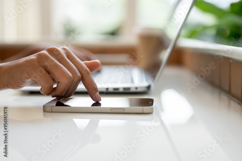 A close-up image of a woman's finger touching on a smartphone screen on a table.