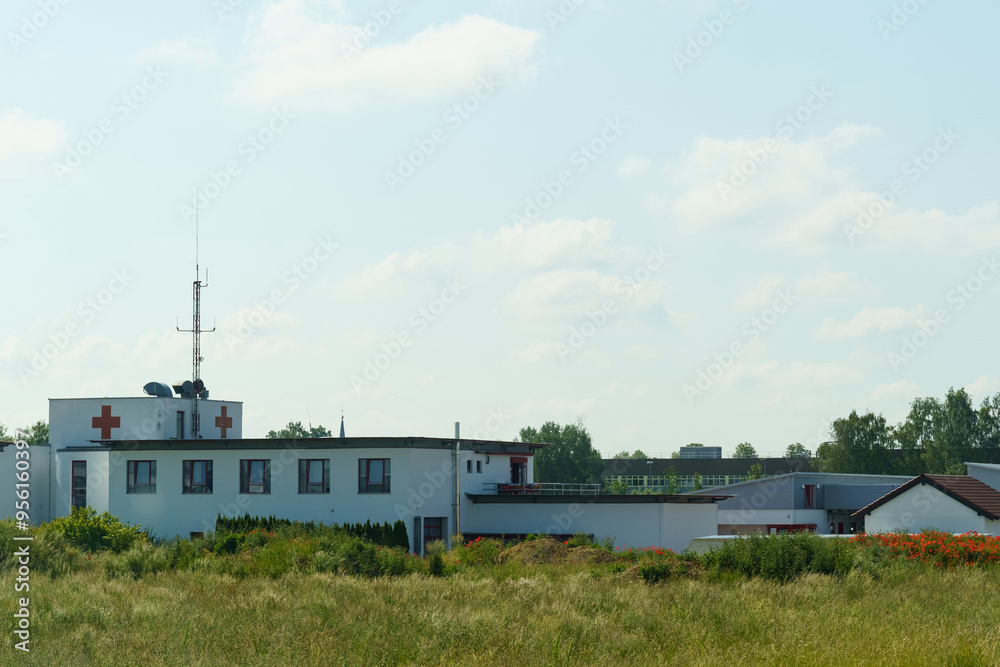 A serene view of a medical building surrounded by greenery on a sunny day with clear skies and distant trees A serene view of a medical building surrounded by greenery on a sunny day with clear skies and distant trees