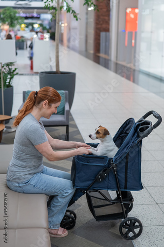 Caucasian woman petting her Jack Russell terrier dog. Shopping with a pet in the mall. Vertical photo.  photo