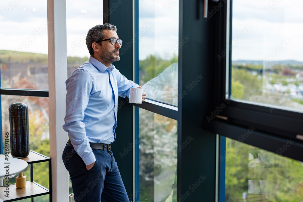 Businessman standing near window with coffee cup at co working space Businessman standing near window with coffee cup at co working space