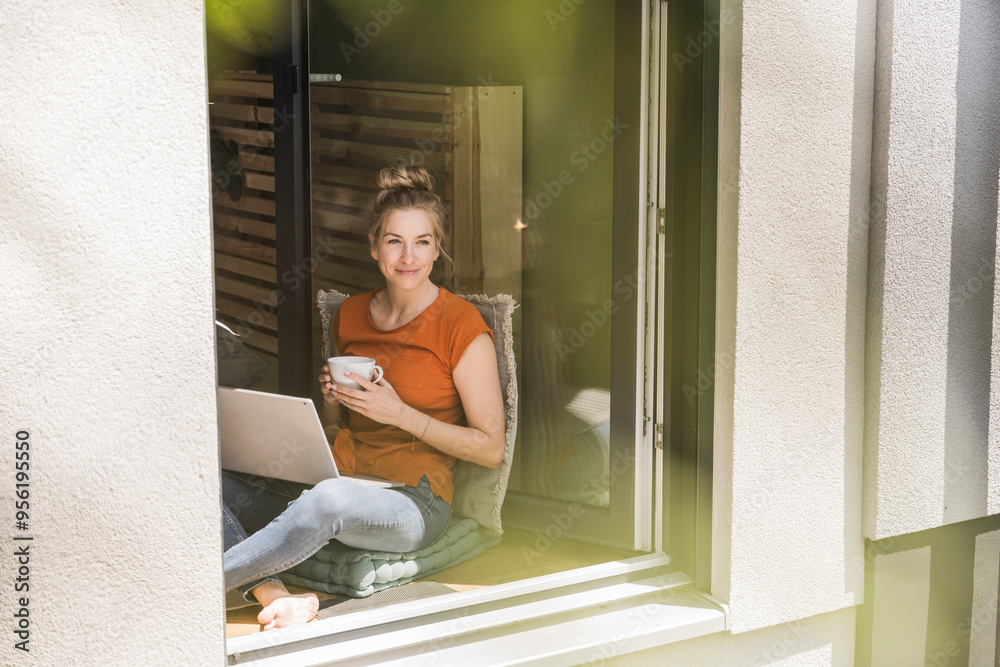 Woman siting by window with laptop and mug Woman siting by window with laptop and mug