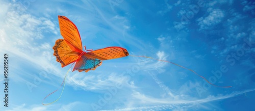 A butterfly shaped toy kite gracefully ascends with its long tail fluttering in the wind at The Knap Barry s family kite festival against a vivid blue sky with scattered clouds perfect for copy space photo