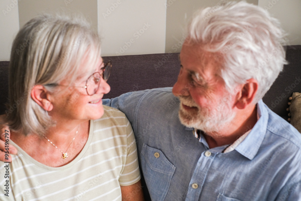 Mature couple sitting on a sofa, lovingly gazing at each other with affection, enjoying their time together at home. Capturing the essence of senior lifestyle, enduring relationships, and love in old Mature couple sitting on a sofa, lovingly gazing at each other with affection, enjoying their time together at home. Capturing the essence of senior lifestyle, enduring relationships, and love in old