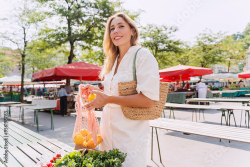 Smiling woman buying lemons in farmer's market on sunny day photo