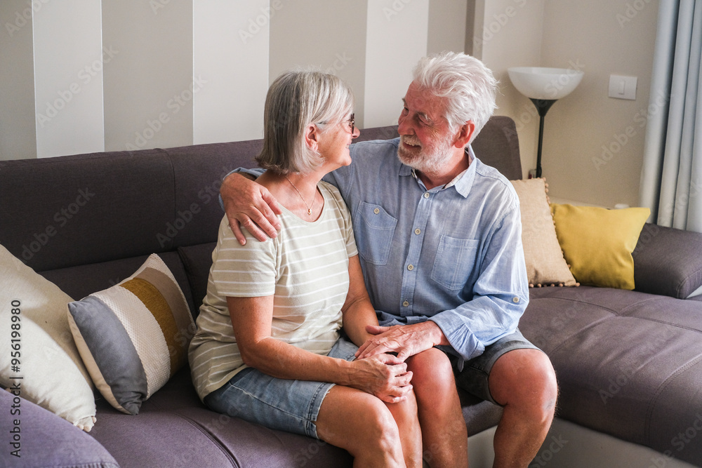 Elderly couple sitting together on a cozy couch at home, smiling and enjoying the warmth of a long-lasting relationship. This heartwarming scene captures the joy and intimacy of a life spent together Elderly couple sitting together on a cozy couch at home, smiling and enjoying the warmth of a long-lasting relationship. This heartwarming scene captures the joy and intimacy of a life spent together