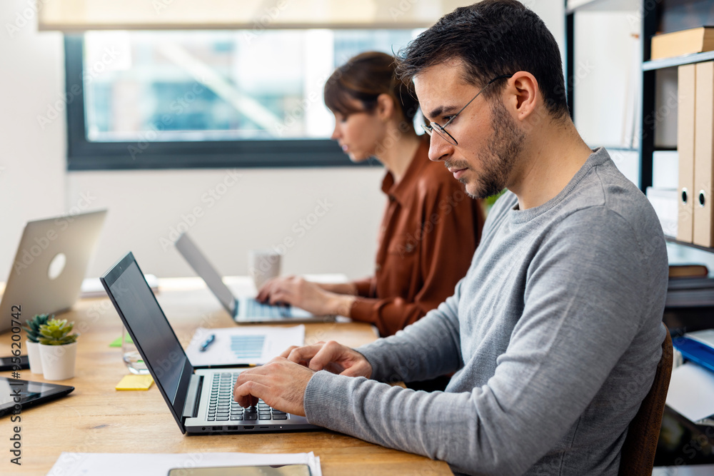 Focused businessman working on laptop and witting with colleague in office Focused businessman working on laptop and witting with colleague in office
