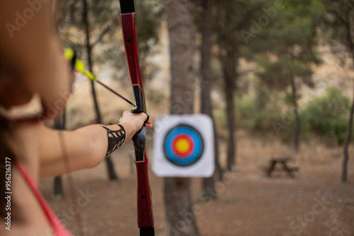 Athlete woman with bow and arrow aiming on sport target board at forest