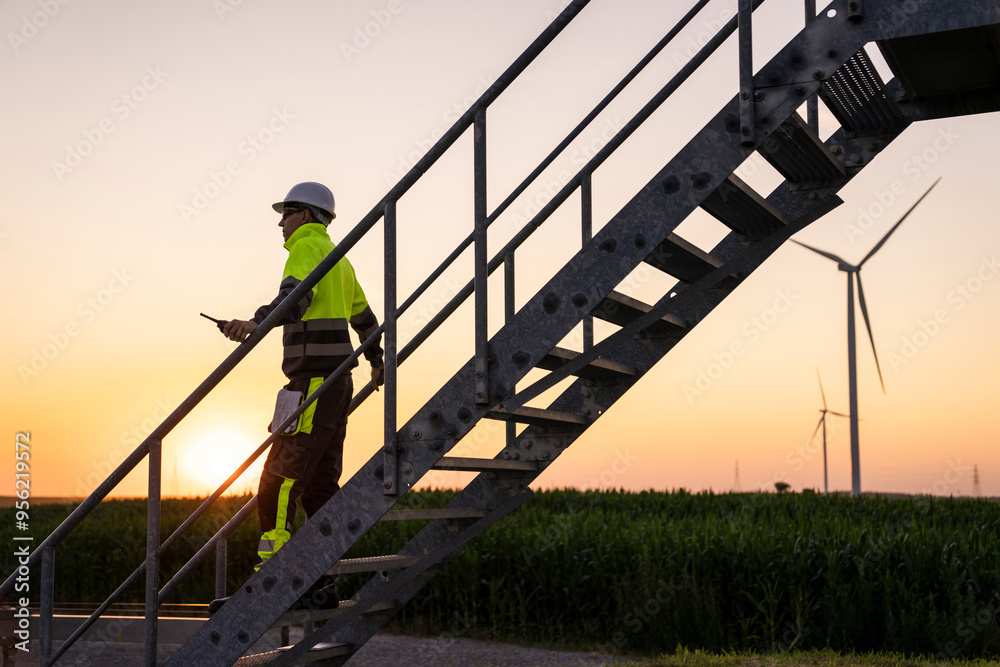 Engineer moving down on stairs by wind turbine field at sunset Engineer moving down on stairs by wind turbine field at sunset