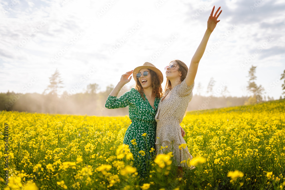 Two friends enjoy a sunny day in a vibrant yellow flower field wearing stylish outfits and sunglasses. Nature, vacation, relax and lifestyle. Summer landscape. Two friends enjoy a sunny day in a vibrant yellow flower field wearing stylish outfits and sunglasses. Nature, vacation, relax and lifestyle. Summer landscape.