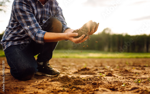 A person kneeling on a farm field analyzing soil quality  in a rural landscape. Garden field ground fertile concept. photo