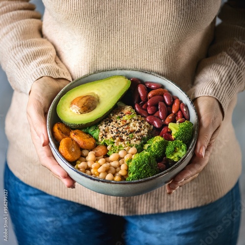 Healthy vegetarian dinner. Woman in jeans and warm sweater holding bowl with fresh salad, avocado, grains, beans, roasted vegetables, close-up. Superfood, clean eating, vegan, dieting food concept