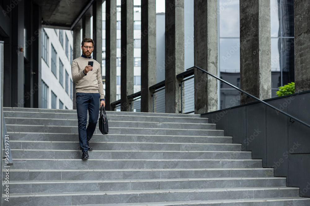 Businessman descends urban stairs while focused on smartphone, demonstrating modern professional life. Dressed in casual business attire, he efficiently multitasks between phone Businessman descends urban stairs while focused on smartphone, demonstrating modern professional life. Dressed in casual business attire, he efficiently multitasks between phone