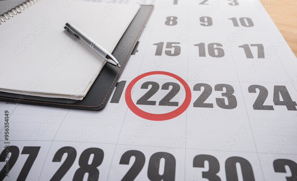 A notebook on a calendar with the 22nd of the month marked with a red circle A notebook on a calendar with the 22nd of the month marked with a red circle