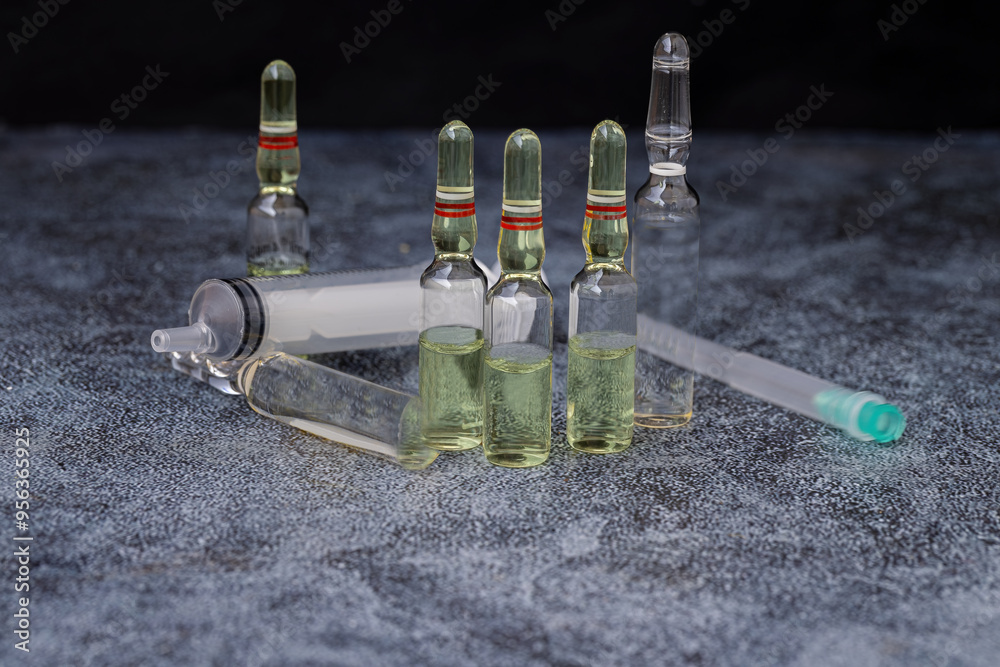 Vaccines, glass ampoules, glass vials containing clear liquid, a syringe, and an insulated hypodermic needle