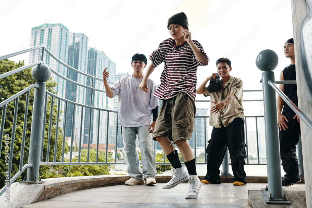 © DragonImages - Group of young men dancing on a balcony, surrounded by urban landscape and city skyscrapers in background. Expressing joy and camaraderie while performing different moves