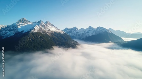 Aerial a rugged mountain range with snow-capped peaks and mist rising from the valleys below, a dramatic and awe-inspiring scene