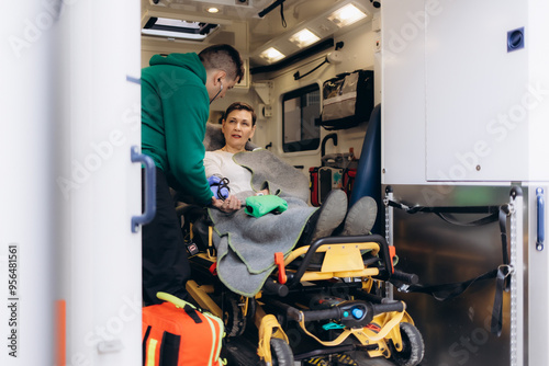 Medics with injured patient giving an infusion . Young male paramedics holding iv solution. Female doctor listeting heart of patient photo