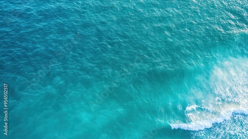 an aerial view of a serene ocean scene with gentle waves rolling towards the shore, the water transitioning from deep blue to light green near the coast