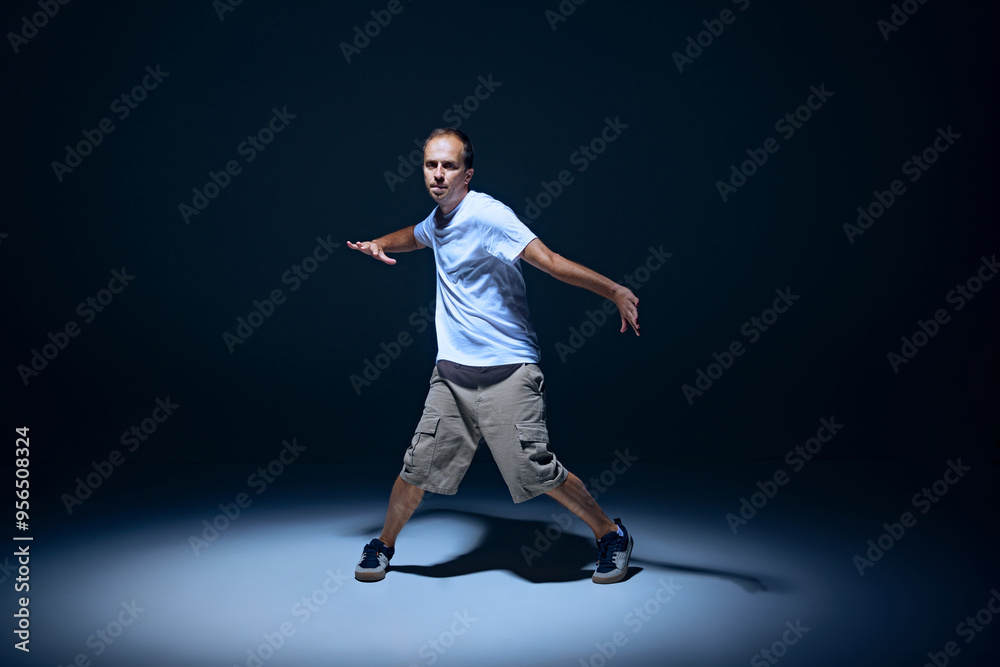Dynamic image of artistic young man in casual clothes dancing hip-hop on stage against black studio background with spotlight. Concept of street style, contemporary dance, entertainment Dynamic image of artistic young man in casual clothes dancing hip-hop on stage against black studio background with spotlight. Concept of street style, contemporary dance, entertainment