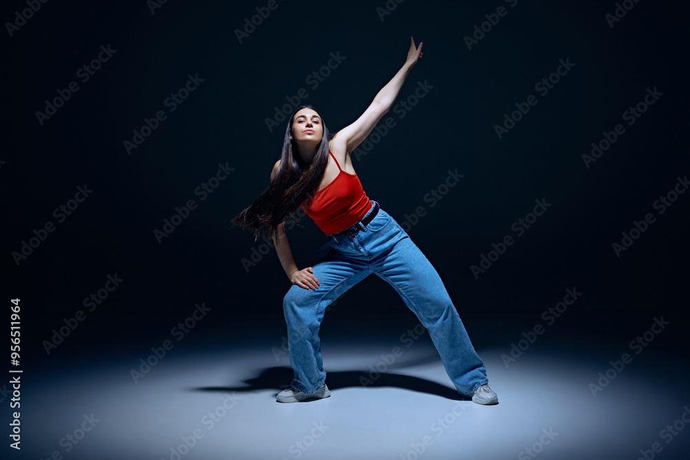 Urban lifestyle. Energetic young woman in jeans and red top performing, dancing hip-hop against black studio background. Concept of street style, contemporary dance, entertainment Urban lifestyle. Energetic young woman in jeans and red top performing, dancing hip-hop against black studio background. Concept of street style, contemporary dance, entertainment