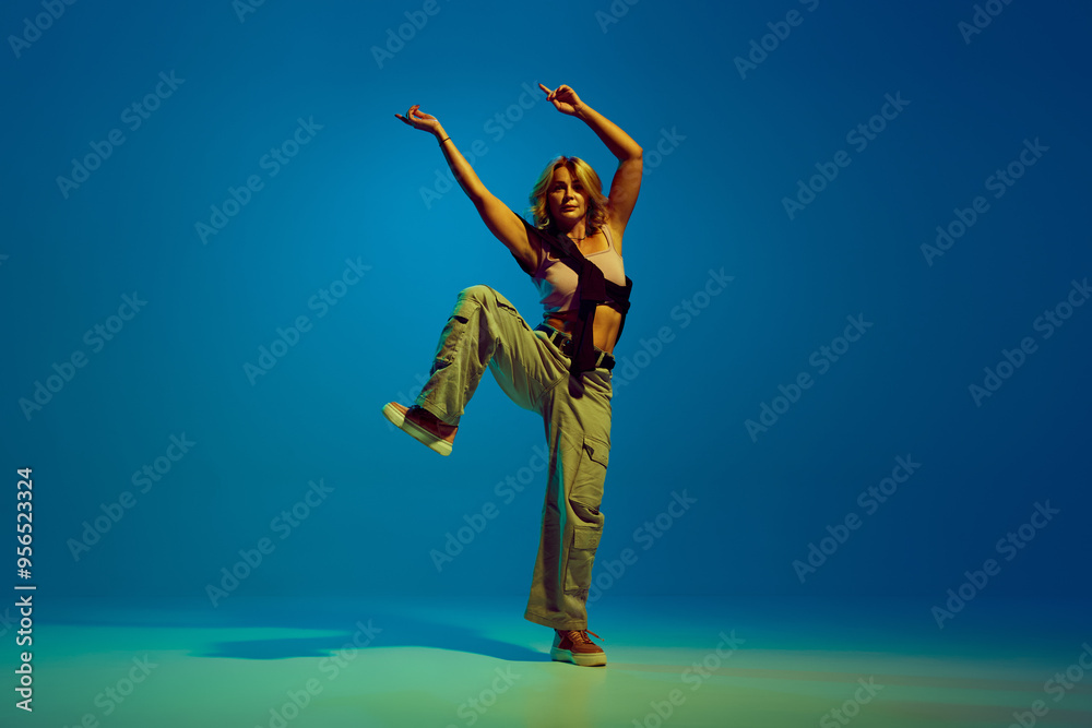 Passionate and artistic dancer, woman in stylish casual clothes making energetic performance, dancing hip-hop against gradient blue background in neon. Concept of street style, contemporary dance Passionate and artistic dancer, woman in stylish casual clothes making energetic performance, dancing hip-hop against gradient blue background in neon. Concept of street style, contemporary dance