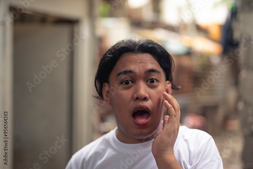 Shot of a young Filipino gay man in his early 20s taken aback mouth wide open gasping in shock. Slum area background.