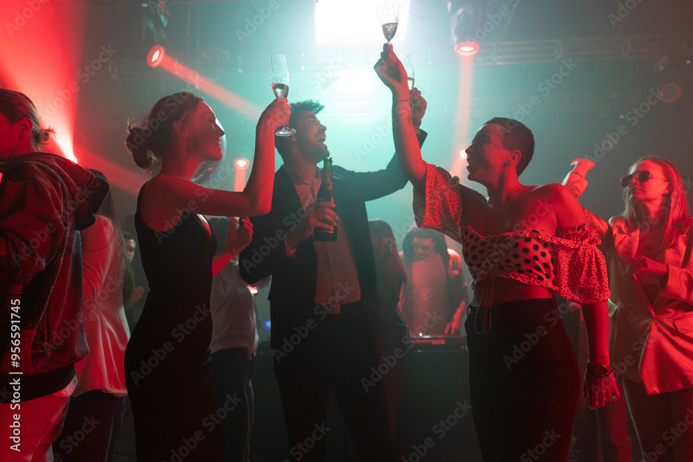 Fototapeta premium Friends at a disco to dance in celebration of new year at a social event with glasses of wine in hands