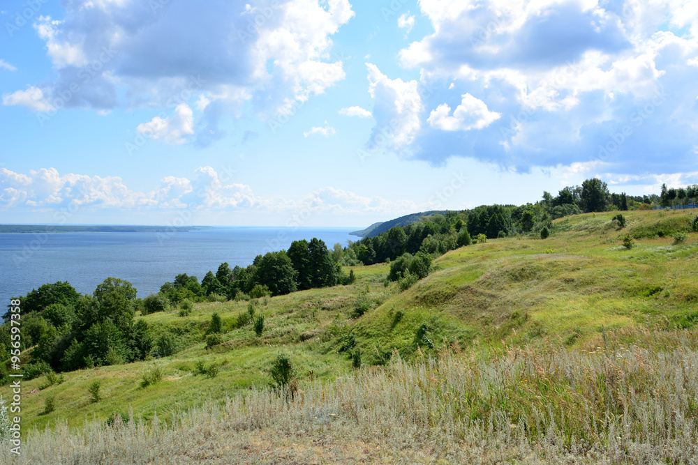 Naklejka premium a hilly coast with a view of a lake and trees and a cloudy sky