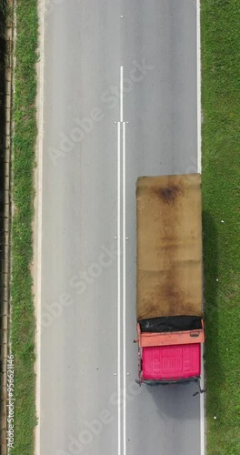 Vertical aerial view of a road with little traffic. View from sky of straight two-lane road. Direct above a paved transport road. White lane markings and gray pavement glow and reflecting in the sun