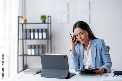 A woman in a blue suit is talking on her cell phone while sitting at a desk