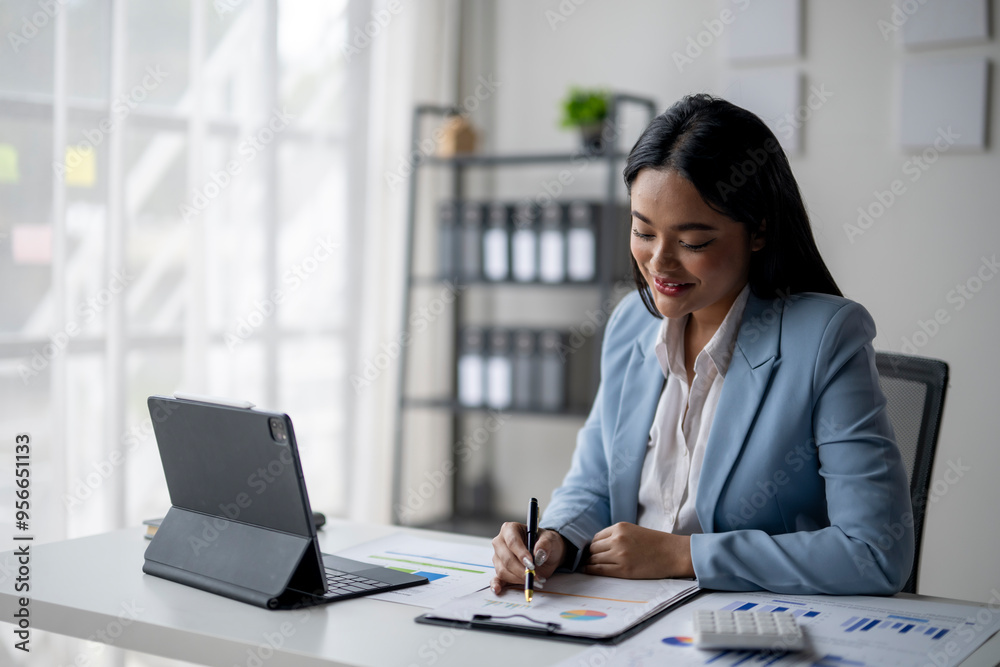 A woman in a blue suit is sitting at a desk with a laptop and a notepad A woman in a blue suit is sitting at a desk with a laptop and a notepad