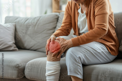 Old woman has knee pain,suffering from pain in leg while sitting on sofa in the living room at home.
