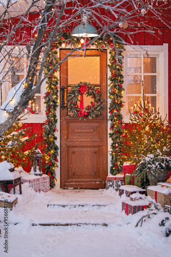 Attractive Christmas entrance decorated with wreath and garlands with snow on the porch.