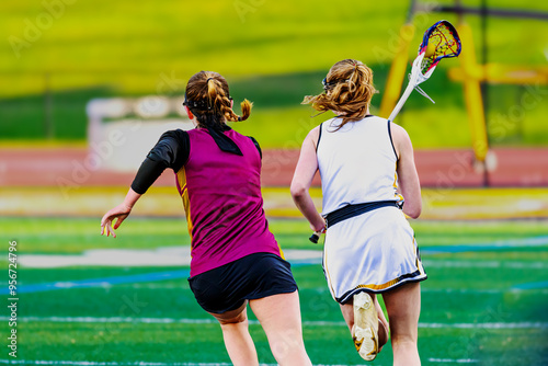 An offensive player with the ball is being chased by the defense. Girls varsity lacrosse game in early Spring in Upstate NY. An athlete takes a hit to the face during this play.