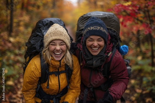 Two friends in warm clothing and backpacks, hiking through a colorful autumn forest, surrounded by vibrant fall foliage, enjoying the crisp air and nature’s beauty on a trail.