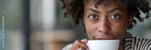 A woman with curly hair holding a white cup, intently savoring her hot beverage as she sits indoors, embodying relaxation and contentment on a quiet, cozy day at home. photo