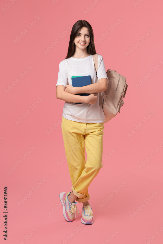 Fototapeta premium Cute teenage girl with backpack and books on pink background